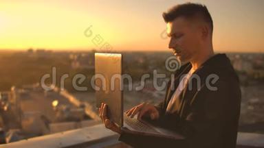 一个有笔记本电脑的<strong>程序员</strong>坐在屋顶上，在日落时写代码。 远程工作自由职业者。 工作自由。 打字